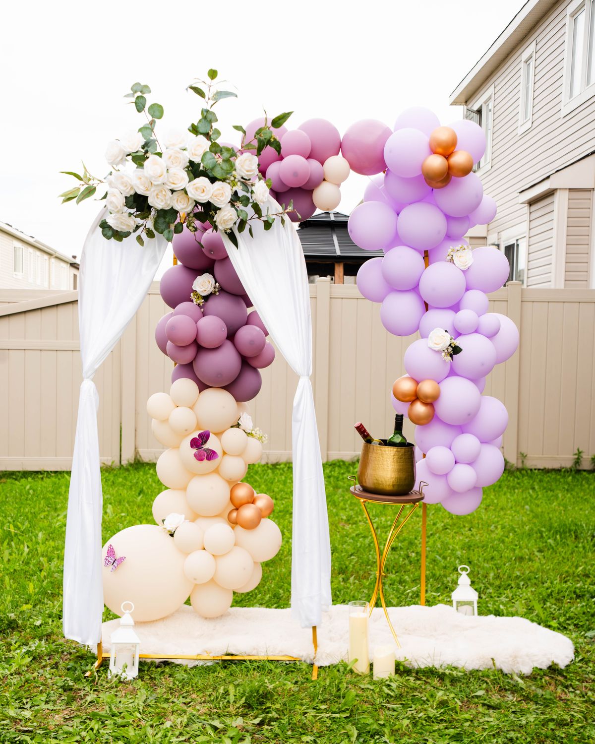 Lilac and mauve balloon arch with white roses and draped fabric in a garden